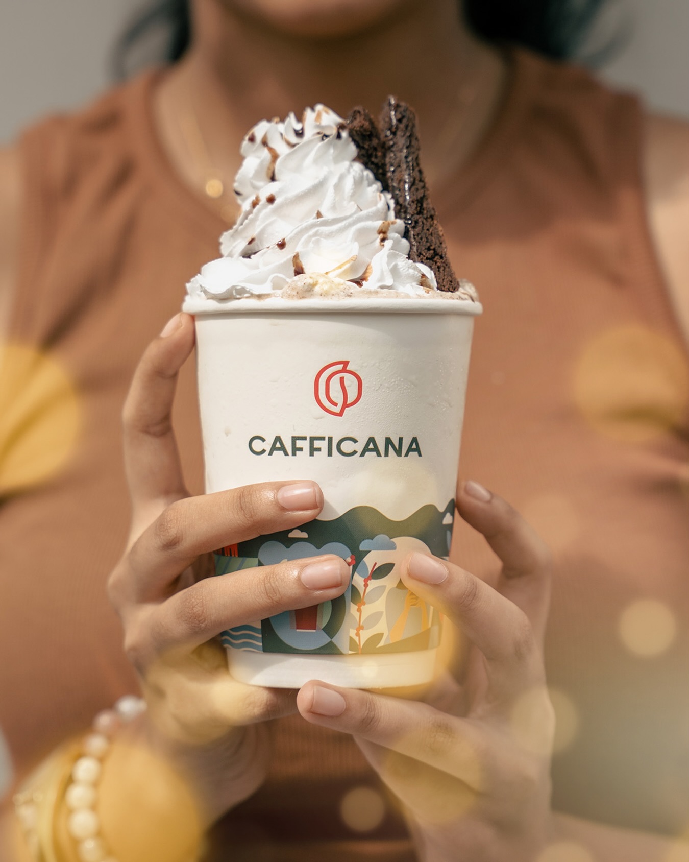 Hands holding a Cafficana paper cup with the illustrated coffee farm design
